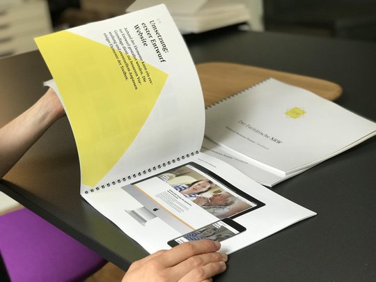 Eine Person blättert durch ein Workbook mit Bildern und Texten. Die Seiten enthalten grafische Elemente und Fotos