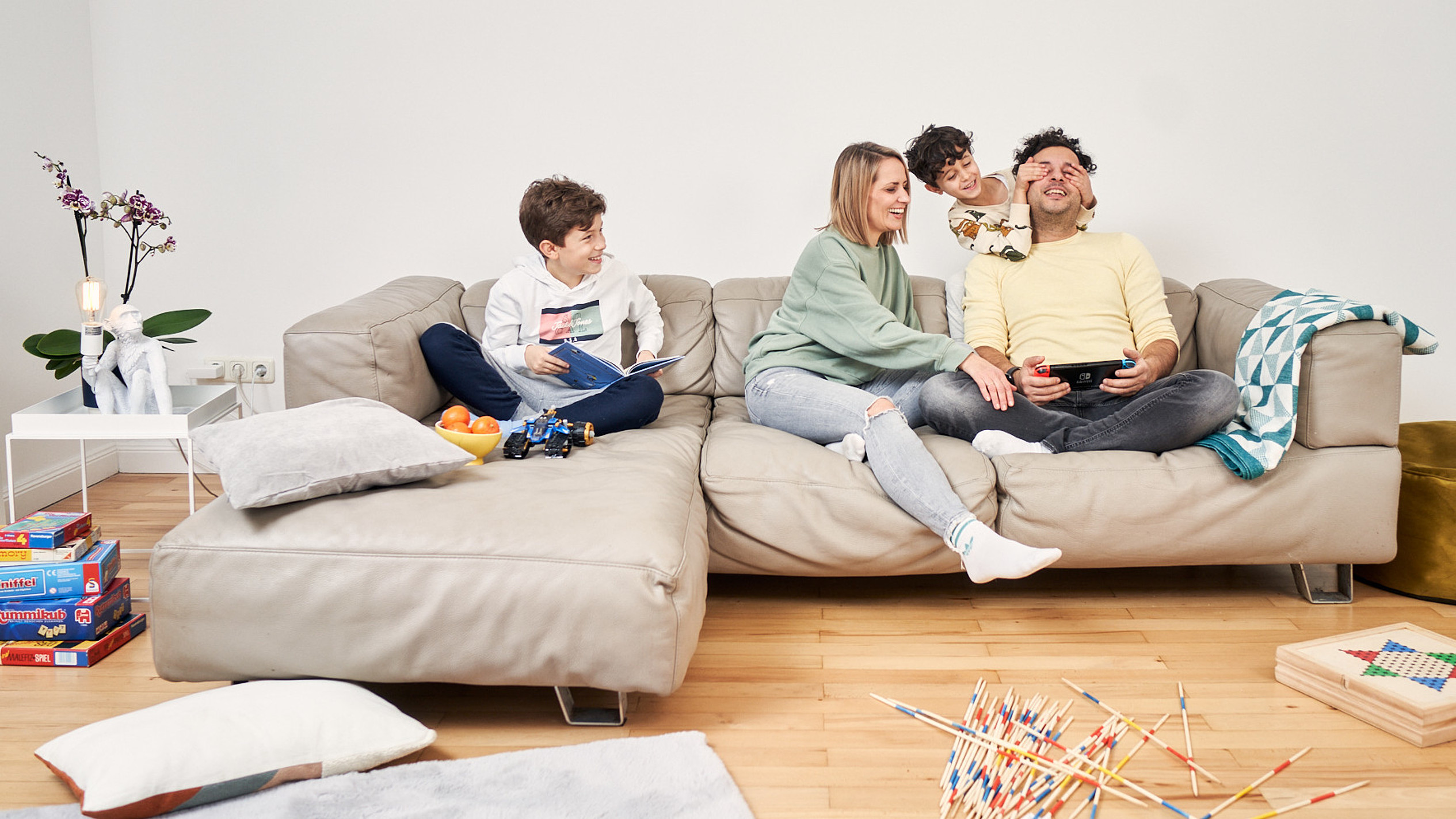 Eine junge Familie mit zwei Kindern spielt auf einem Sofa.