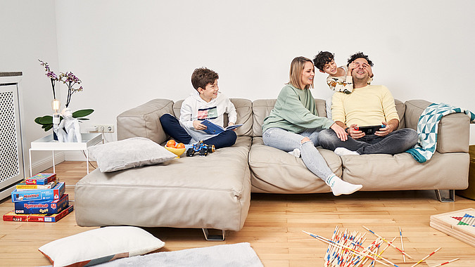 Eine junge Familie mit zwei Kindern spielt auf einem Sofa.