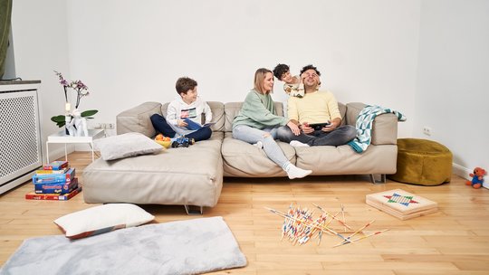 Eine junge Familie mit zwei Kindern spielt auf einem Sofa.