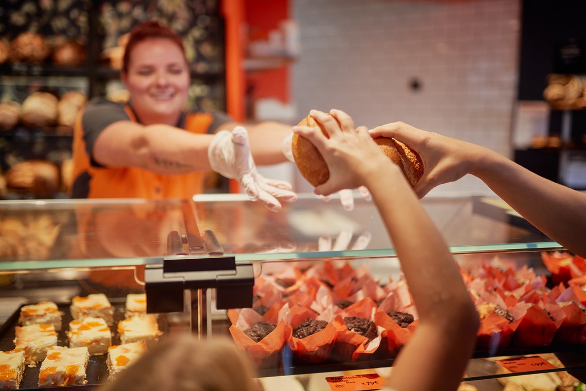 Bäckereiverkäuferin reicht Brot über die Theke an einen Kunden.