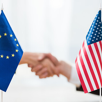EU und USA Fahne auf Tisch, im Hintergrund werden Hände geschüttelt