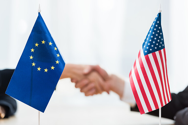 EU und USA Flagge, im Hintergrund ein Händeschütteln