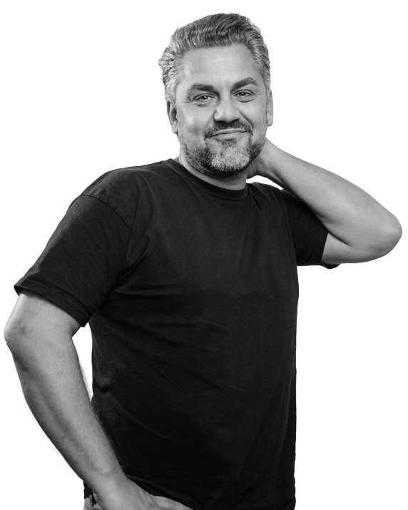 Mann in schwarzem T-Shirt lächelt, Hand am Nacken, grauer Hintergrund.