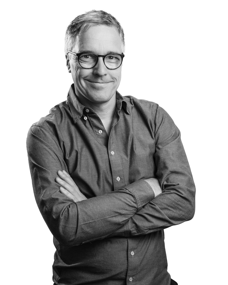 Mann mit Brille und grauem Hemd lächelt mit verschränkten Armen.