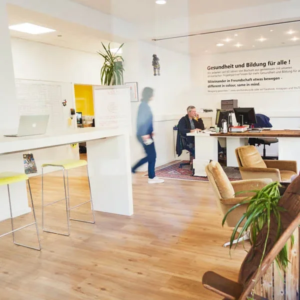 Modernes Büro mit Schreibtisch, Pflanzen und Personen im Gespräch.