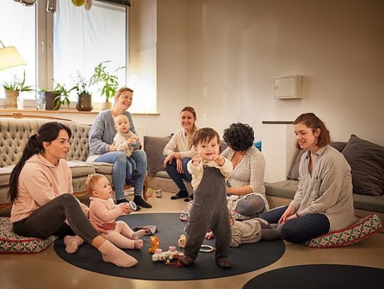 Eine Gruppe Mütter mit Kleinkindern sitzt fröhlich im Spielbereich des ANNA.