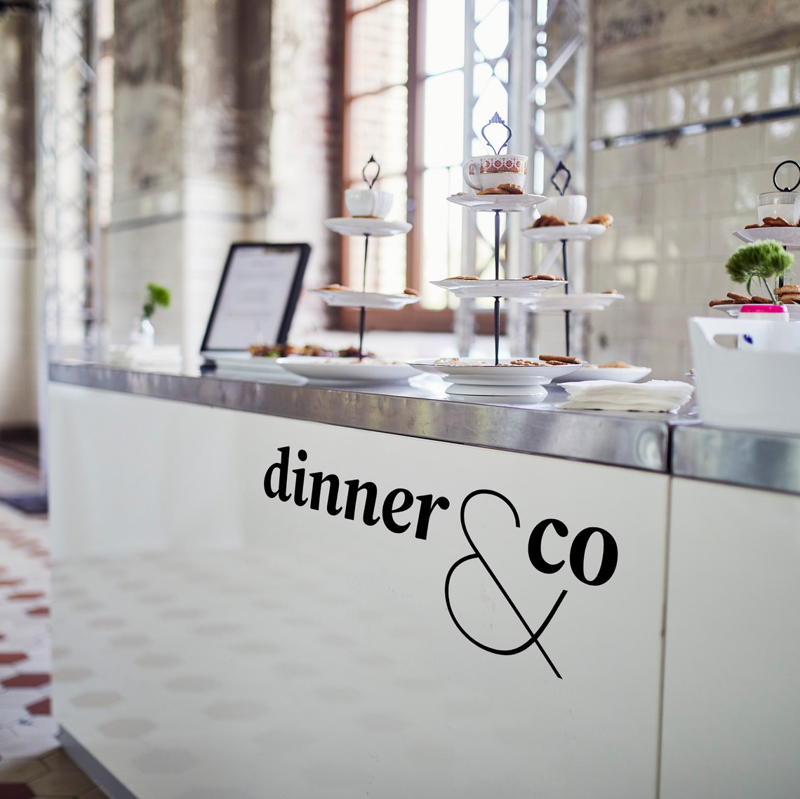 Buffettisch mit Etagere und Geschirr, Markenzeichen „dinner & co“ auf der Tischfront.