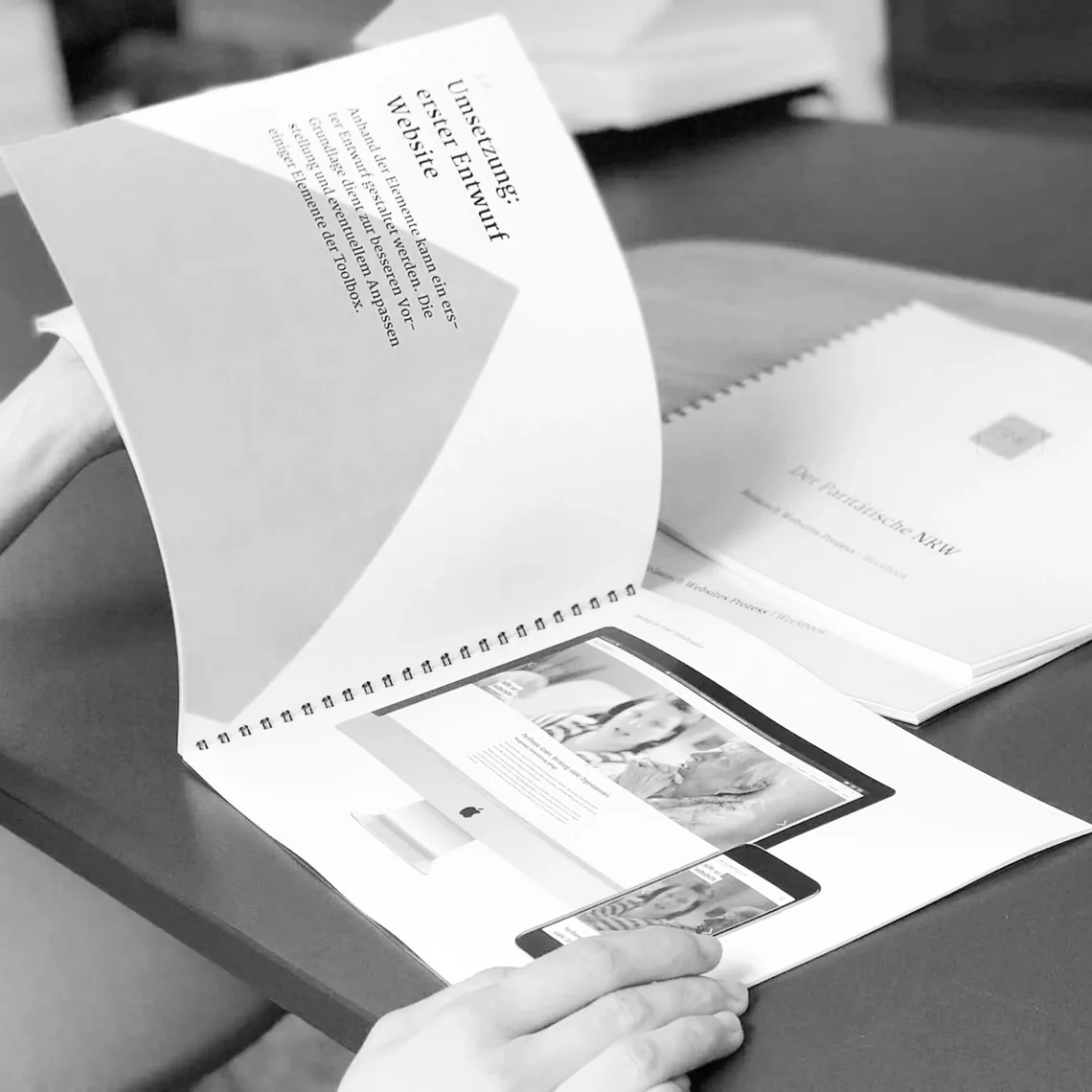 Person blättert durch Heft über Website-Entwurf auf einem Tisch.