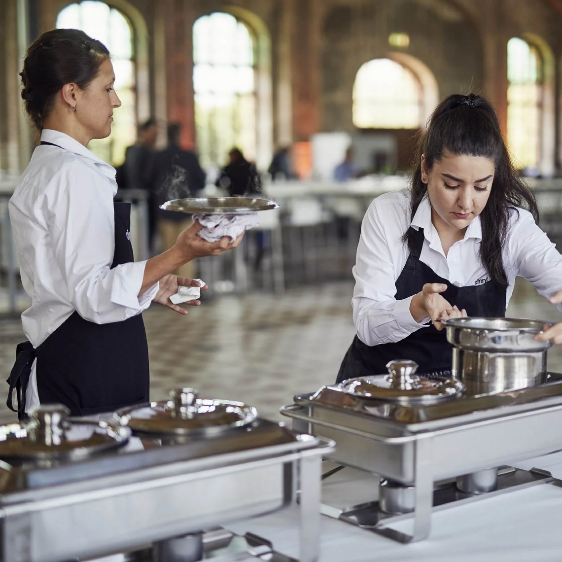 Zwei Kellnerinnen bereiten ein Buffet in einem großen Raum vor.