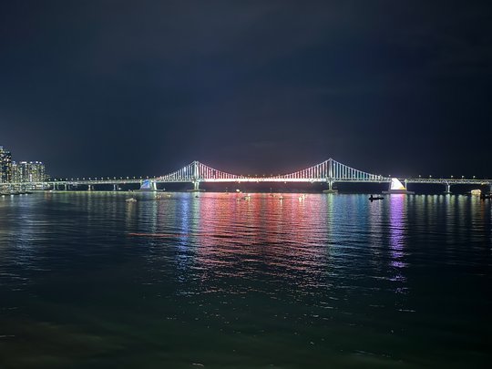 Bei Nacht beleuchtete Gwangan-Brücke. Die Beleuchtung ändert sich ständig und kleine Animationen werden abgespielt. Außerdem gibt es in der Bucht oft Feuerwerk von den vielen kleinen Touristen und Fischer Booten aus