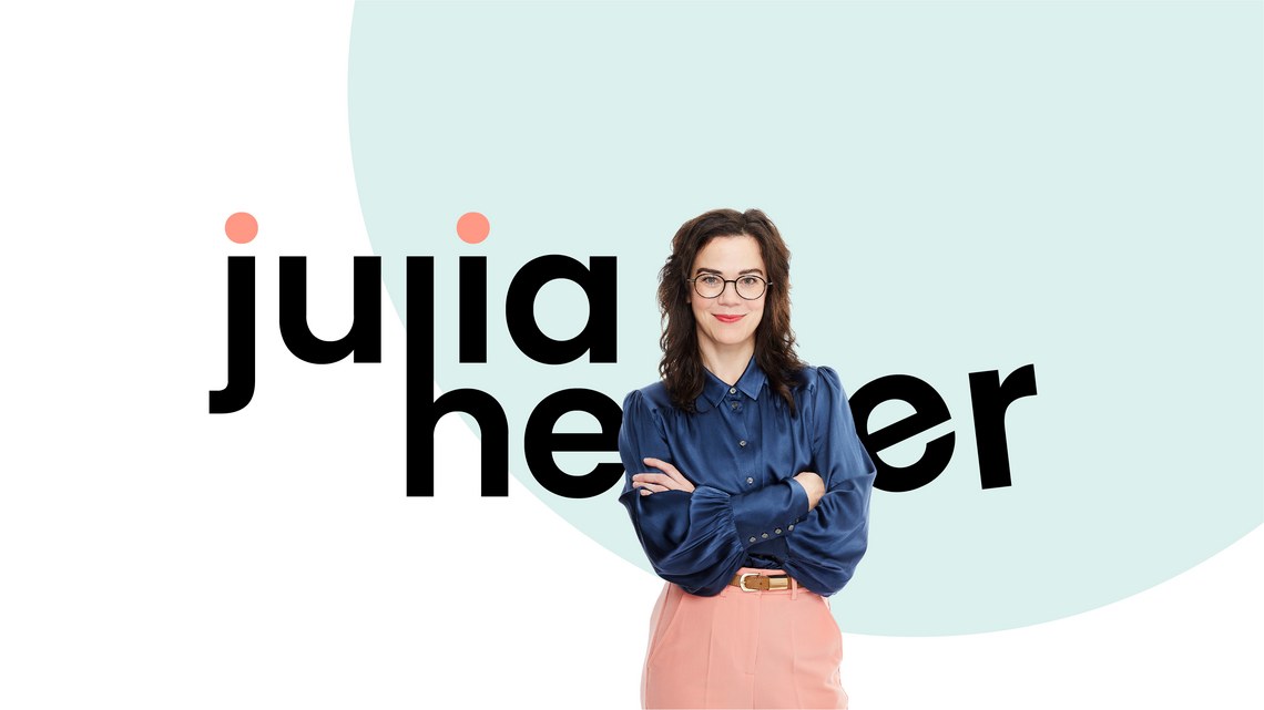 Frau mit Brille und blauem Hemd vor großem Schriftzug auf hellem Hintergrund.