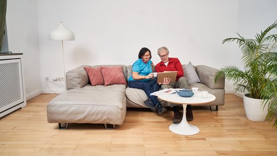 Ein attraktives Best-Ager Paar sitzt auf einem Sofa und schaut gemeinsam auf ein iPad.