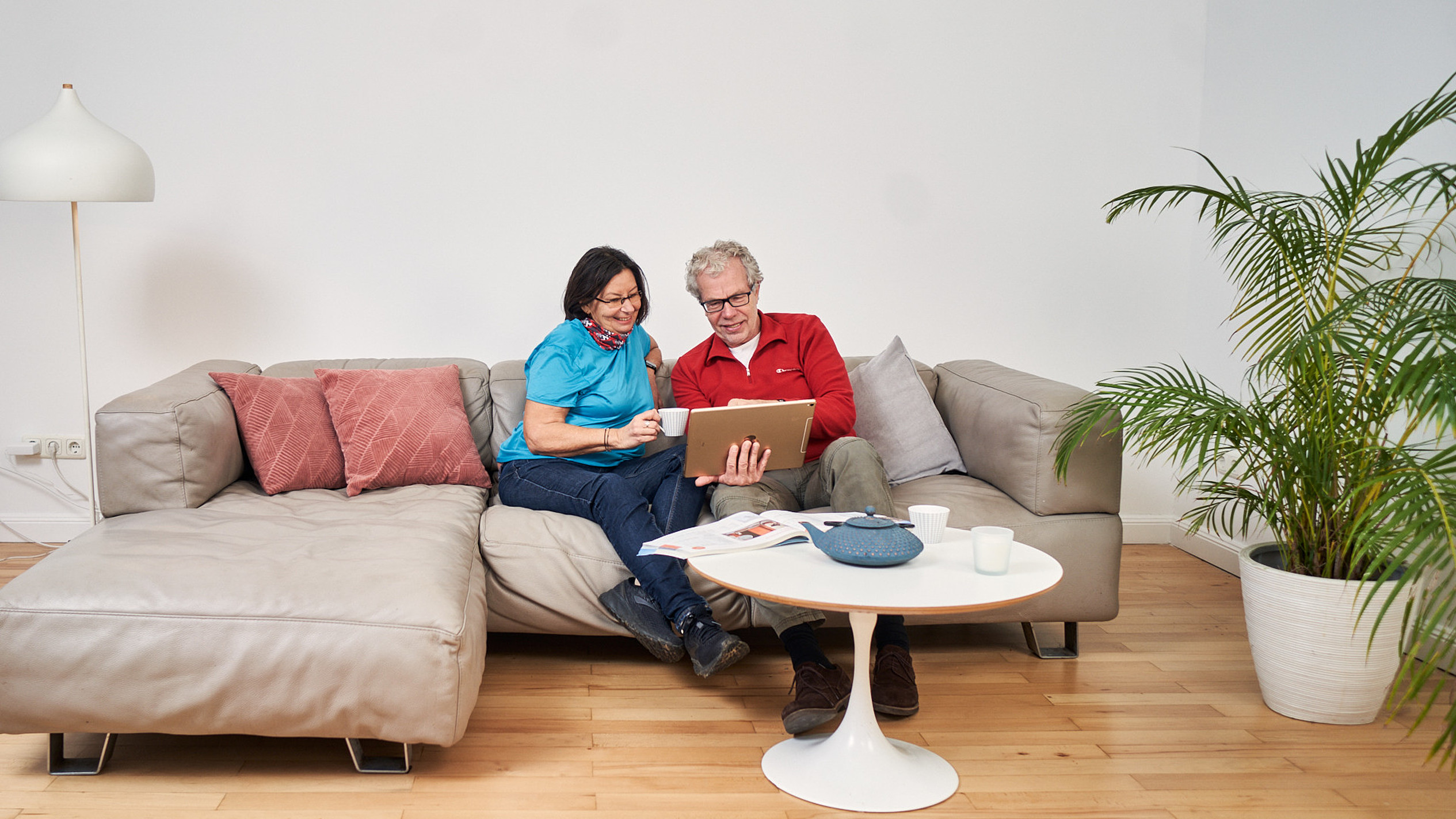Ein attraktives Best-Ager Paar sitzt auf einem Sofa und schaut gemeinsam auf ein iPad.