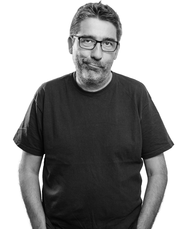 Mann mit Brille und Bart in dunklem Shirt vor weißem Hintergrund.