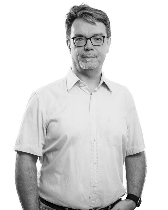 Mann mit Brille in hellblauem Hemd und Jeans vor weißem Hintergrund.