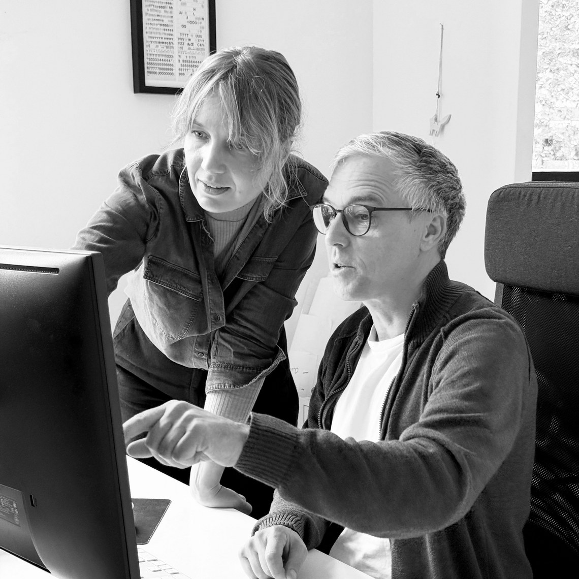 Zwei Personen arbeiten konzentriert an einem Computermonitor.