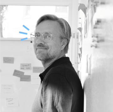 Mann mit Brille lächelt vor einer Wand mit Notizen.